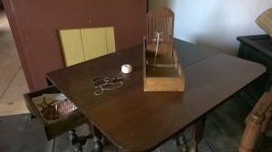 A very small hand loom, likely used by a young girl to weave long fabric tapes. These tapes were in high demand in colonial households for their usefulness in binding things together, as well as adjusting the fit of clothes as a money saver.